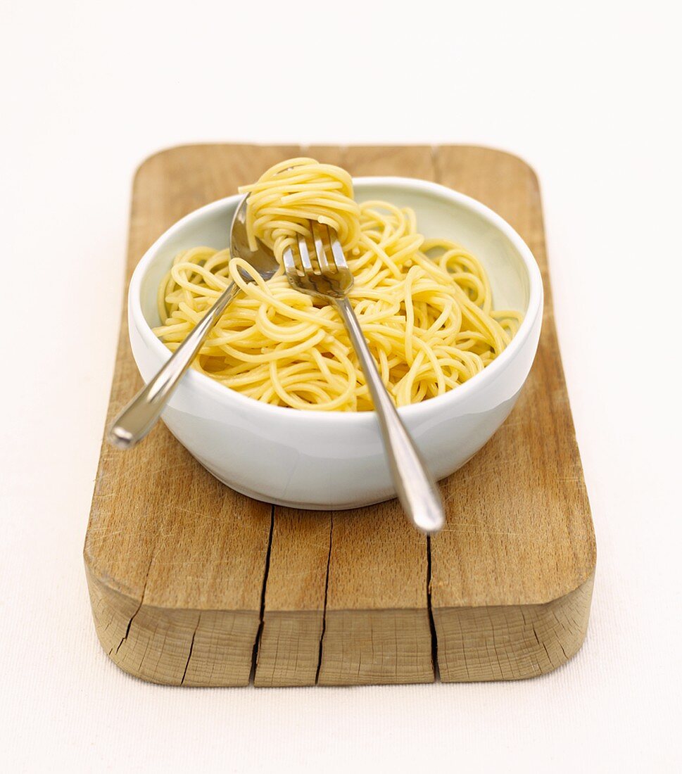 Schüssel mit gekochten Spaghetti auf einem Holzbrett