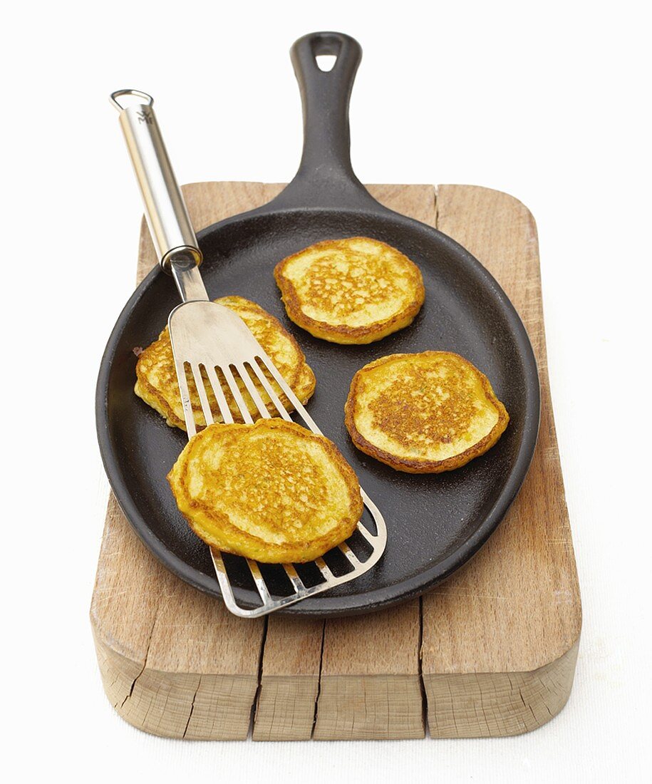 Small corn pancakes in frying pan on a wooden board