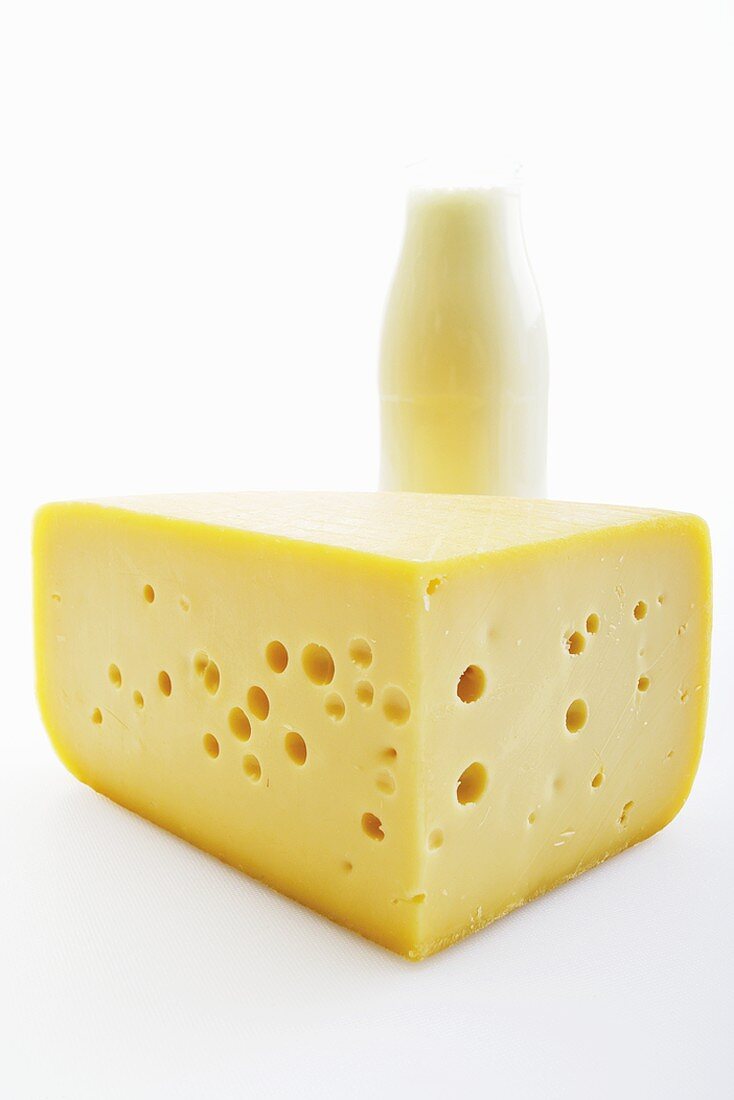 A piece of cheese with a bottle of milk in the background