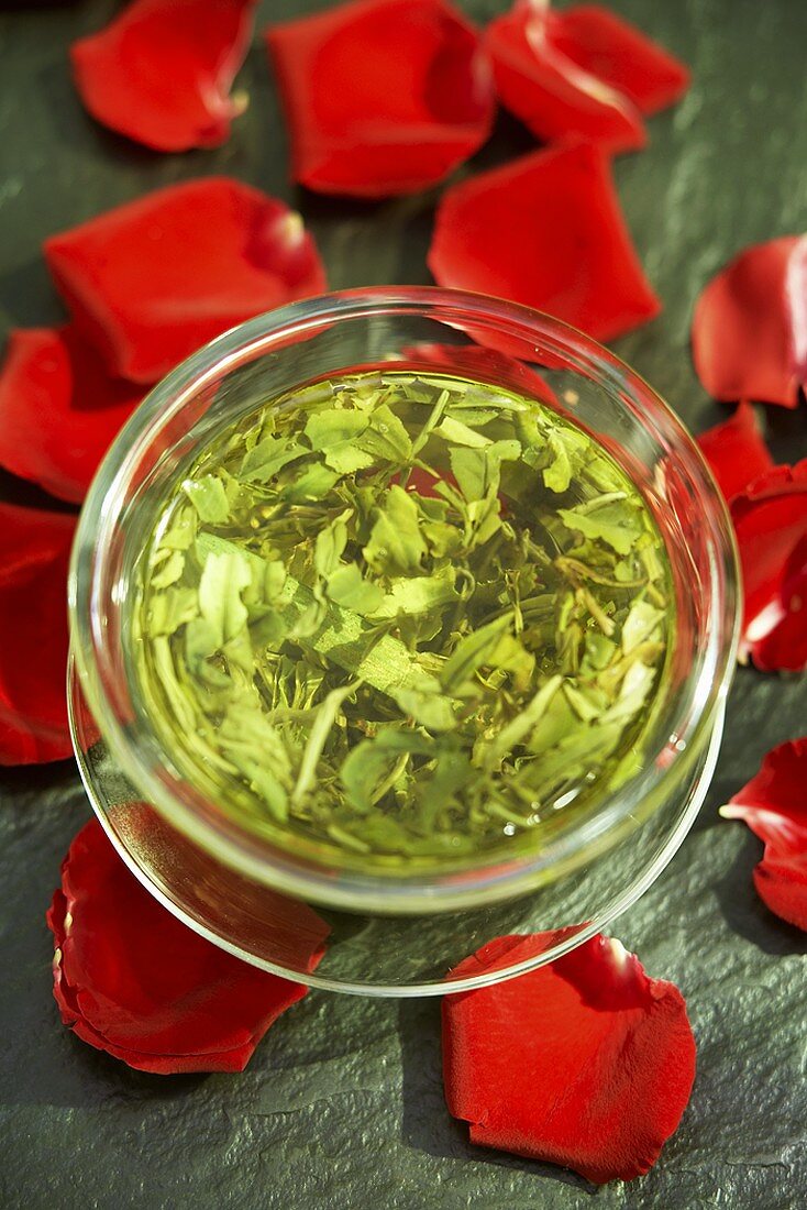 Grüner Tee - Aufguss umgeben von roten Rosenblättern