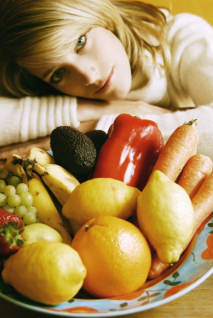 Junge Frau sitzt vor einem Obst und Gemüseteller