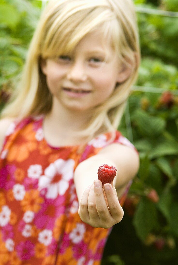 Blond girl holding a raspberry in her hand