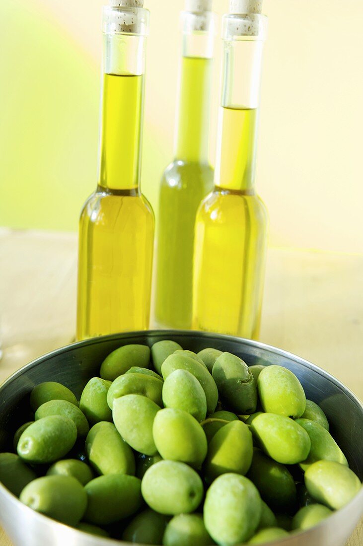 Grüne Oliven in einer Schüssel und Olivenöl dahinter