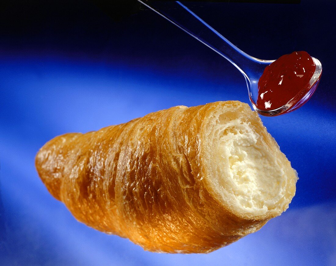 Ein Croissant mit Himbeermarmelade auf einem Löffel