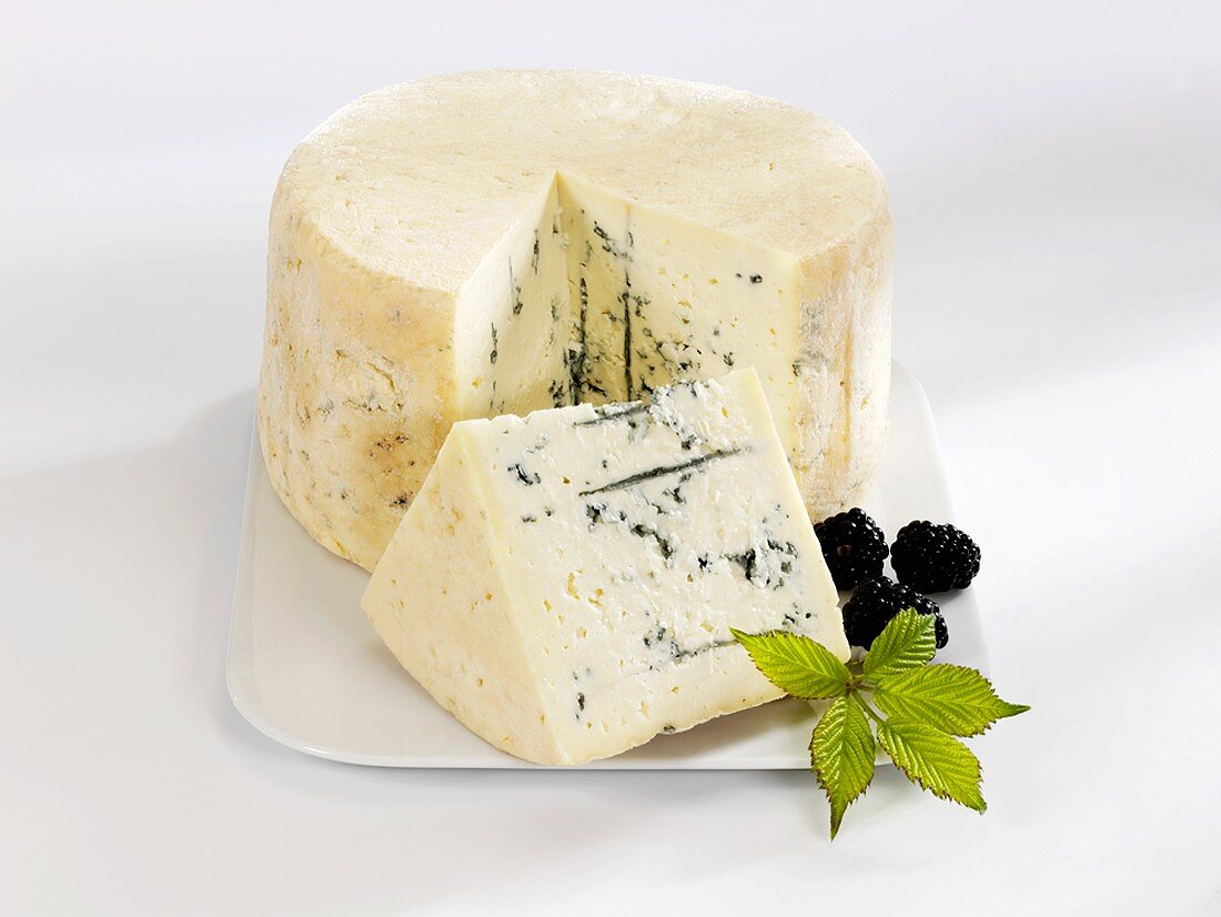 A blue cheese with a piece cut and blackberries