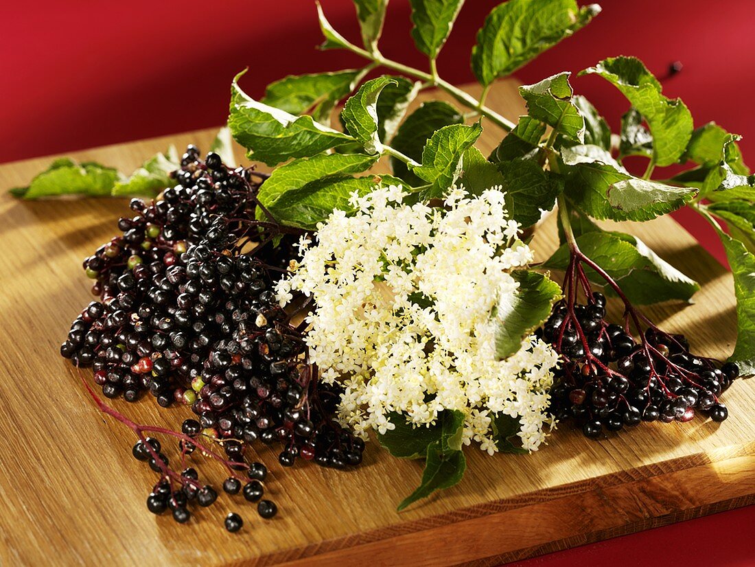 Frische Holunderbeeren und Holunderblüten auf einem Holzbrett