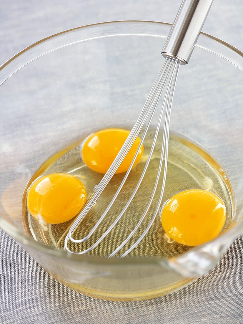 Drei aufgeschlagene Eier in Glasschüssel mit Schneebesen