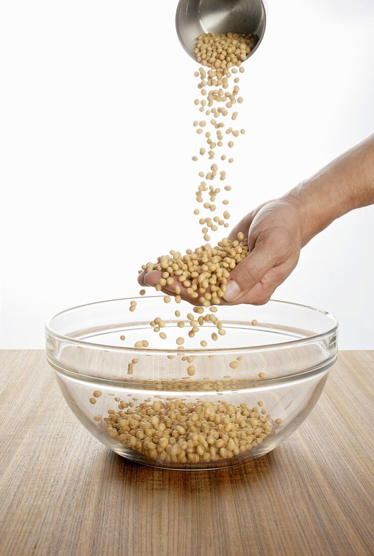 Someone pouring soya beans over their hand into a glass bowl