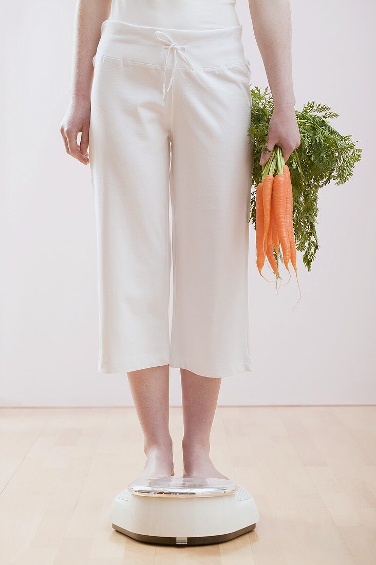 Young woman with carrots on bathroom scales