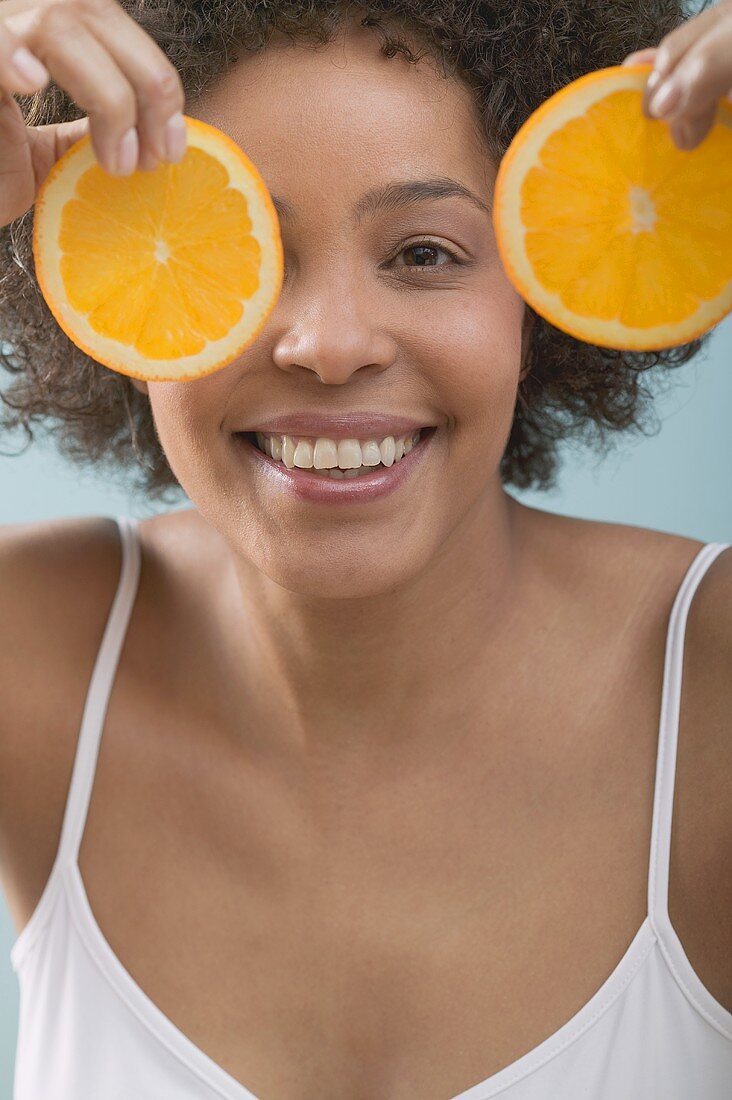 Junge Frau mit Orangenscheiben vor Gesicht