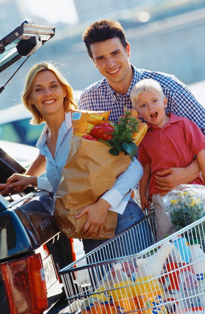 Family food shopping with shopping trolley next to car