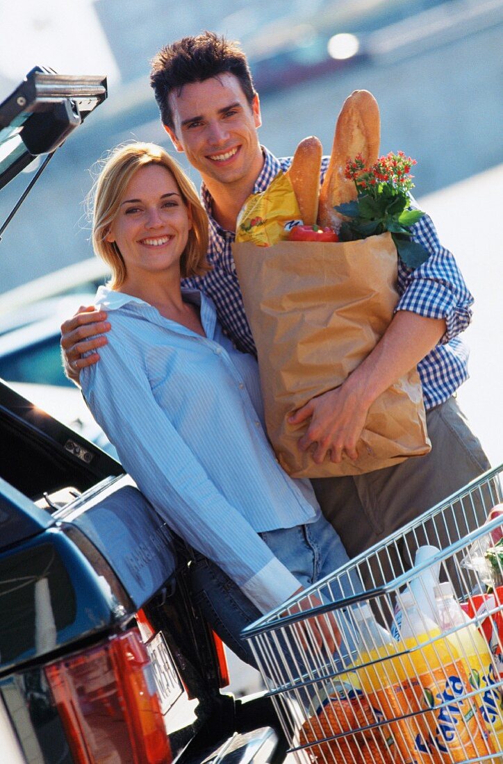 Couple food shopping with shopping trolley next to car