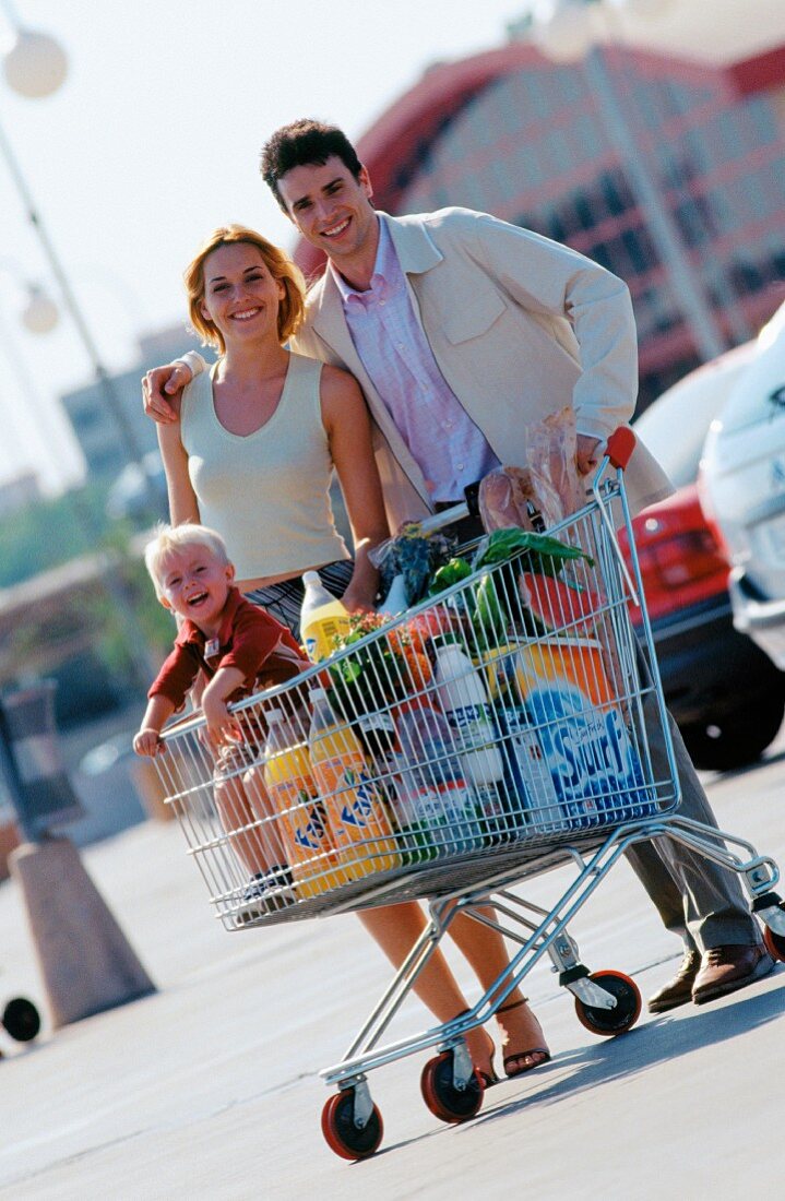 Familie mit Einkaufswagen auf Parkplatz vor dem Supermarkt