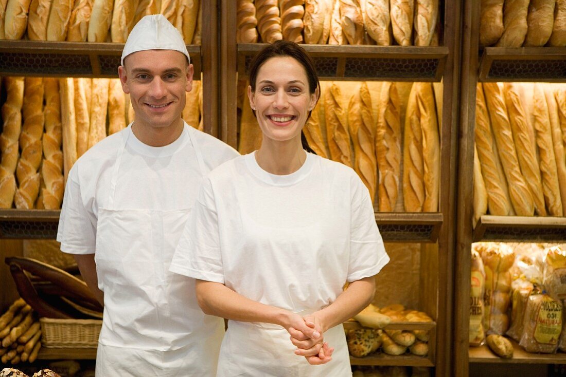 Baker and sales assistant in bakery with racks of baguettes