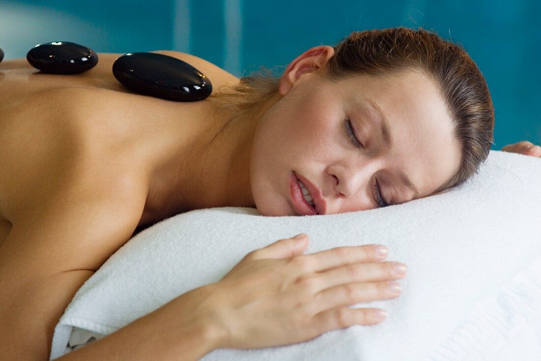 Woman lying on massage table with pebbles on back (LaStone therapy)