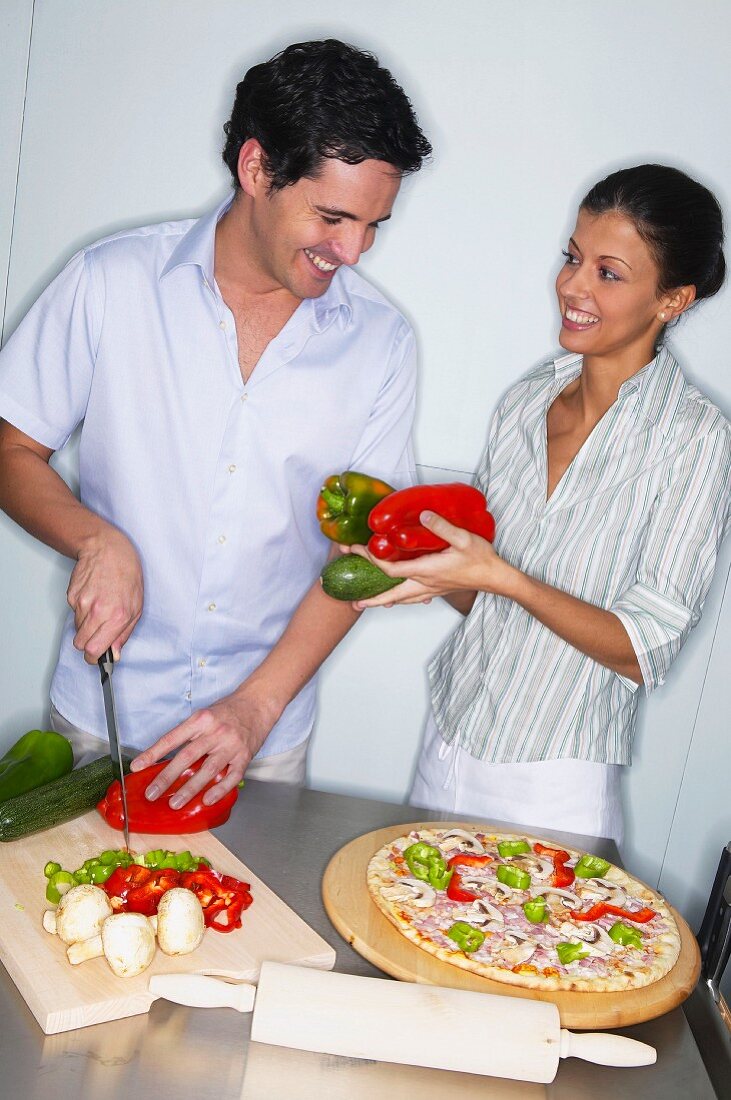 Couple topping a pizza in kitchen