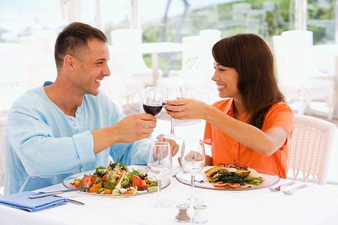 Couple on holiday clinking wine glasses over lunch