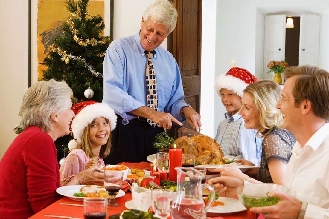 Family eating Christmas dinner, grandfather carving the turkey