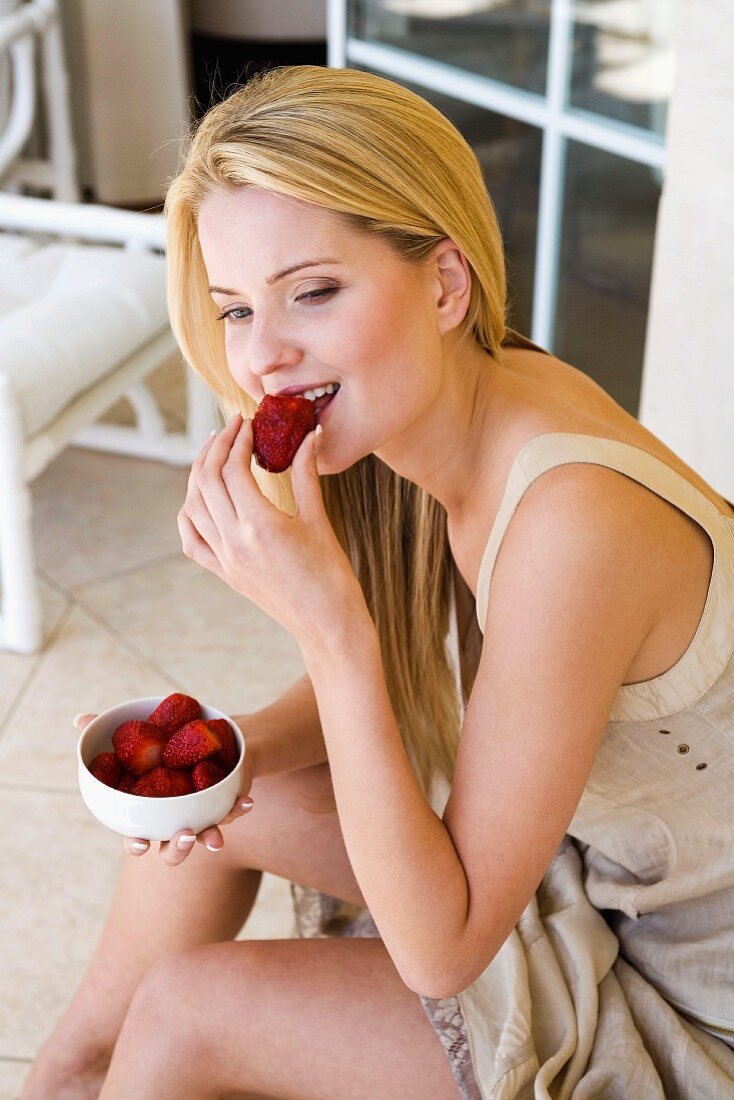 Blonde Frau isst sitzend Erdbeeren