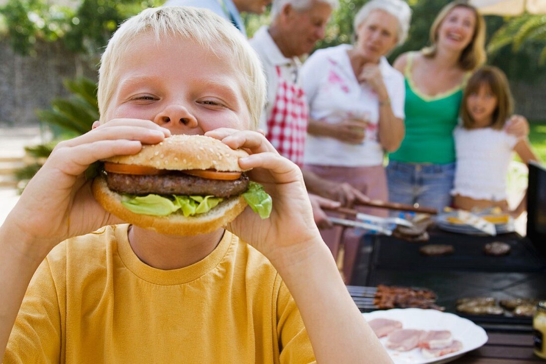 Junge beisst in einen ganzen selbstgemachten Hamburger