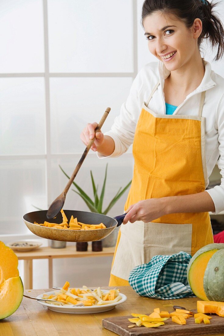 Woman in apron frying pumpkin in pan