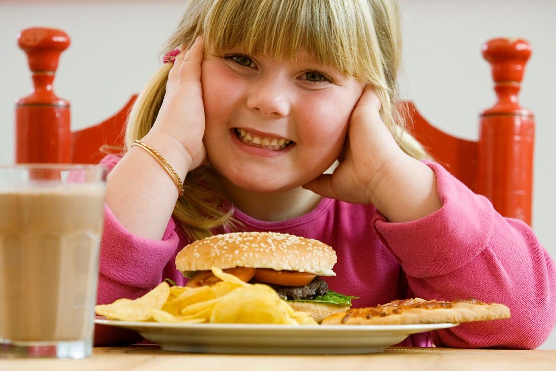 Girl sitting in front of plate of hamburger and crisps