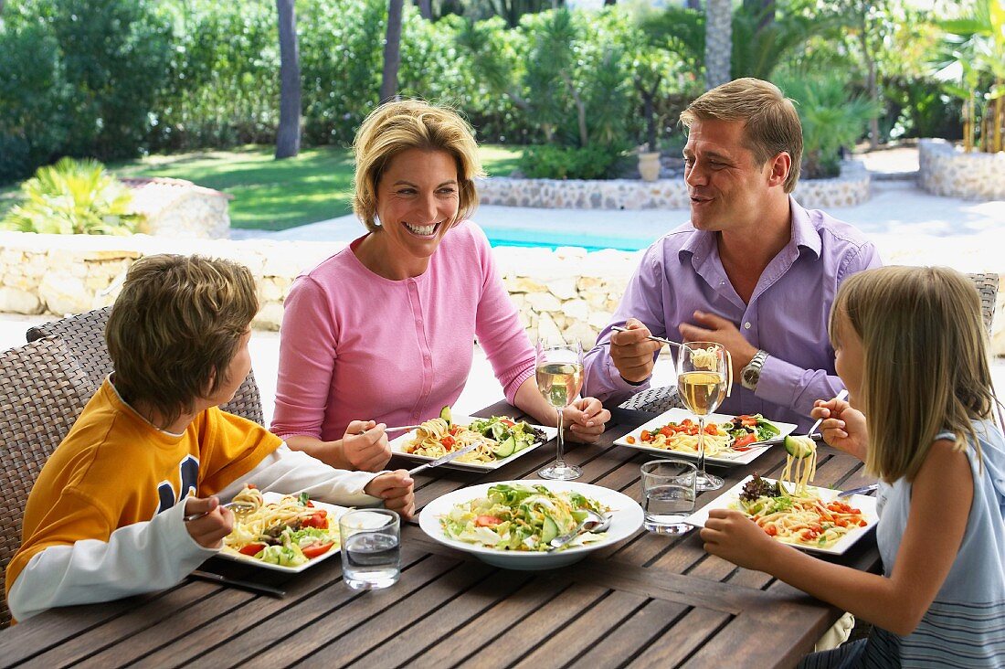 Familie beim Mittagessen mit Salat und Nudeln im Urlaub