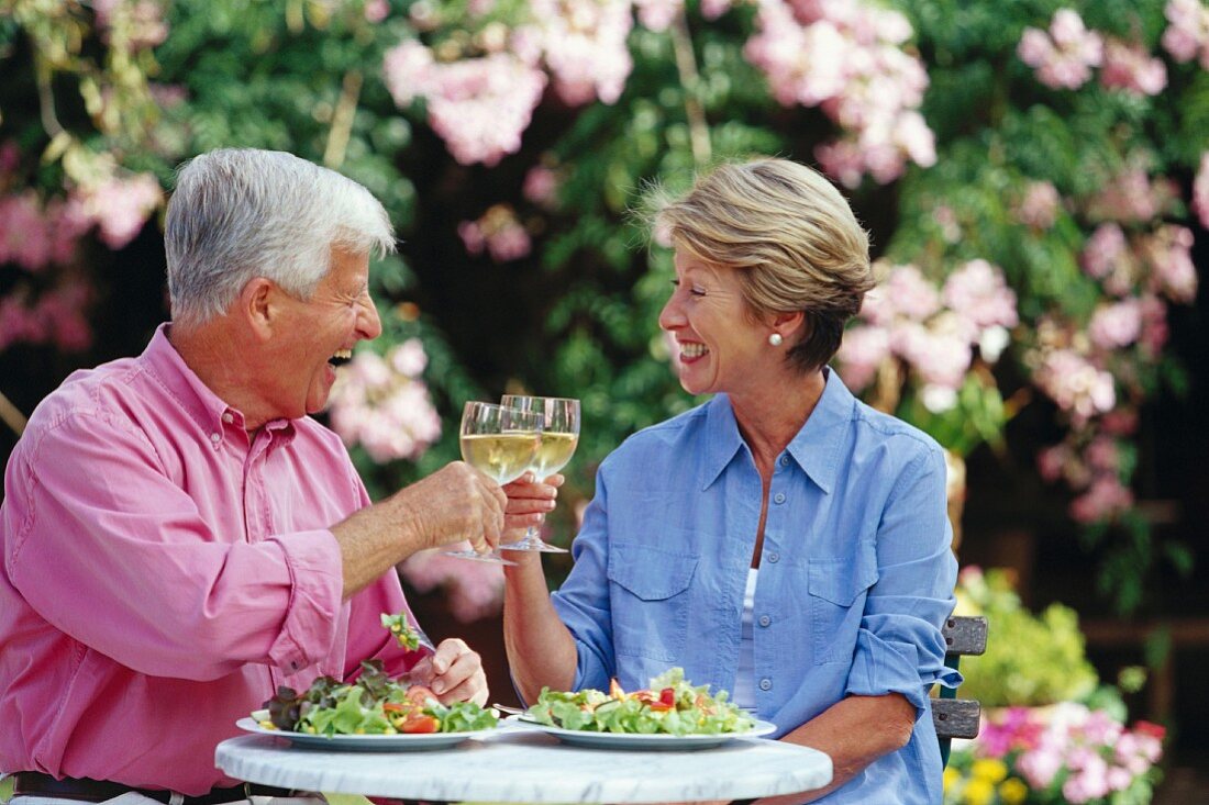 Older married couple clinking glasses of white wine