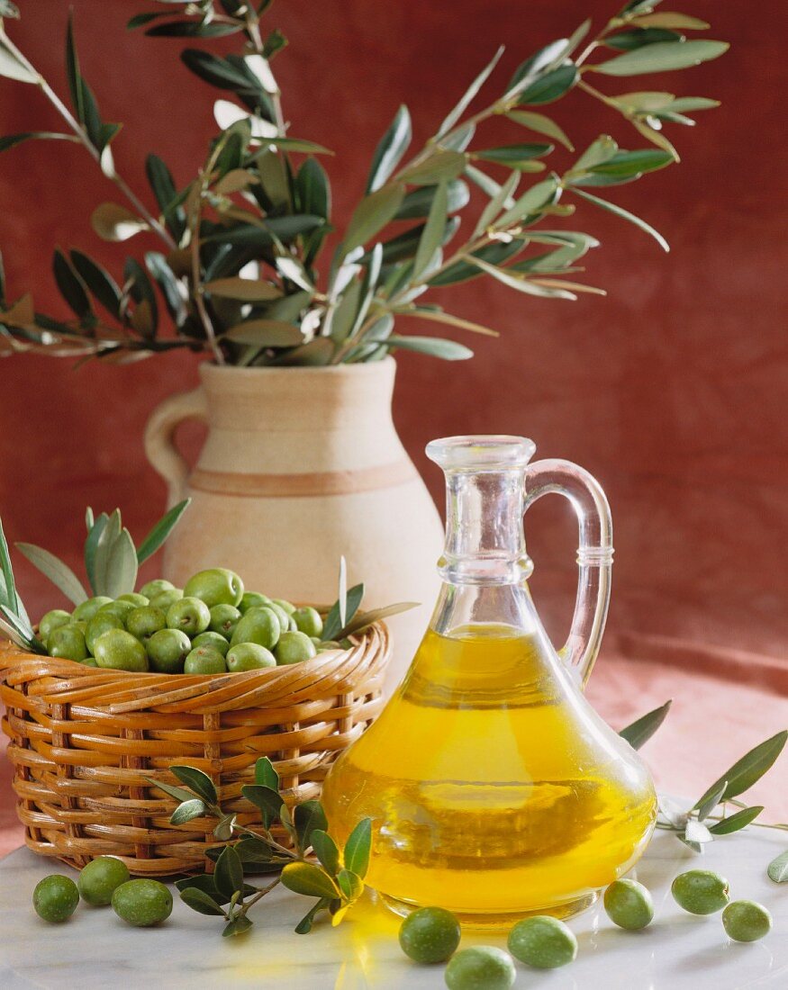 Olive oil with freshly harvested green olives in front of olive branches