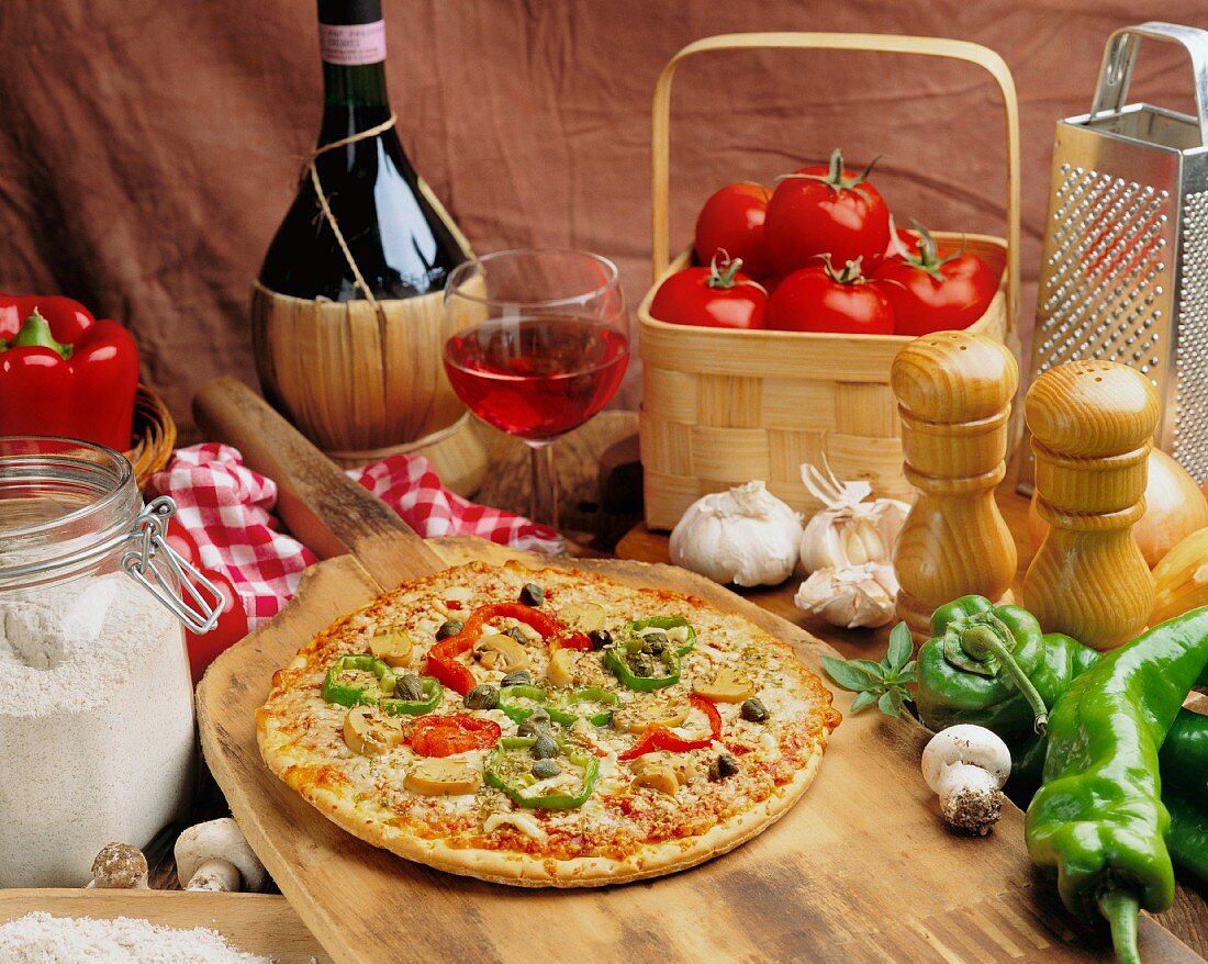 Gemüsepizza frisch aus dem Ofen mit Zutaten und einem Glas Wein
