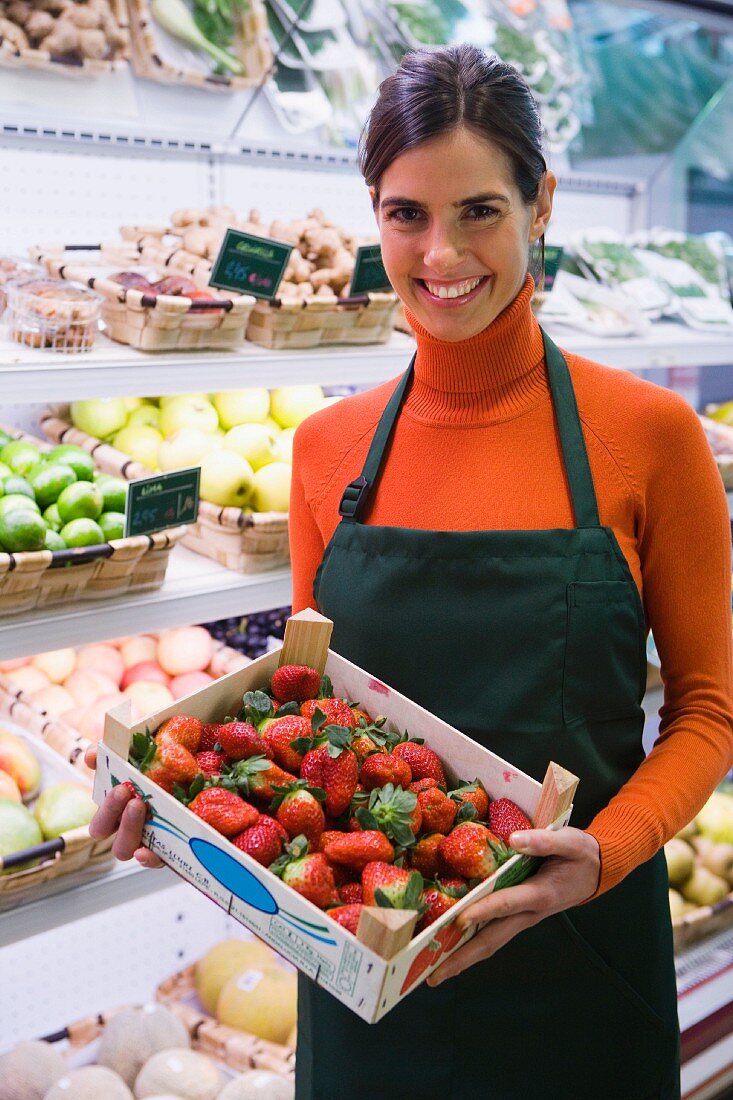 Sales assistant in front of fruit racks with crate of strawberries
