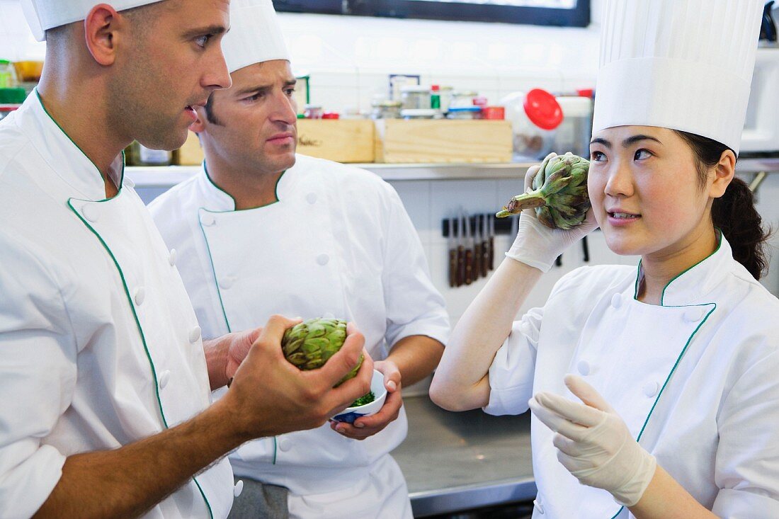 A head chef explaining to a trainee how to check that an artichoke is fresh