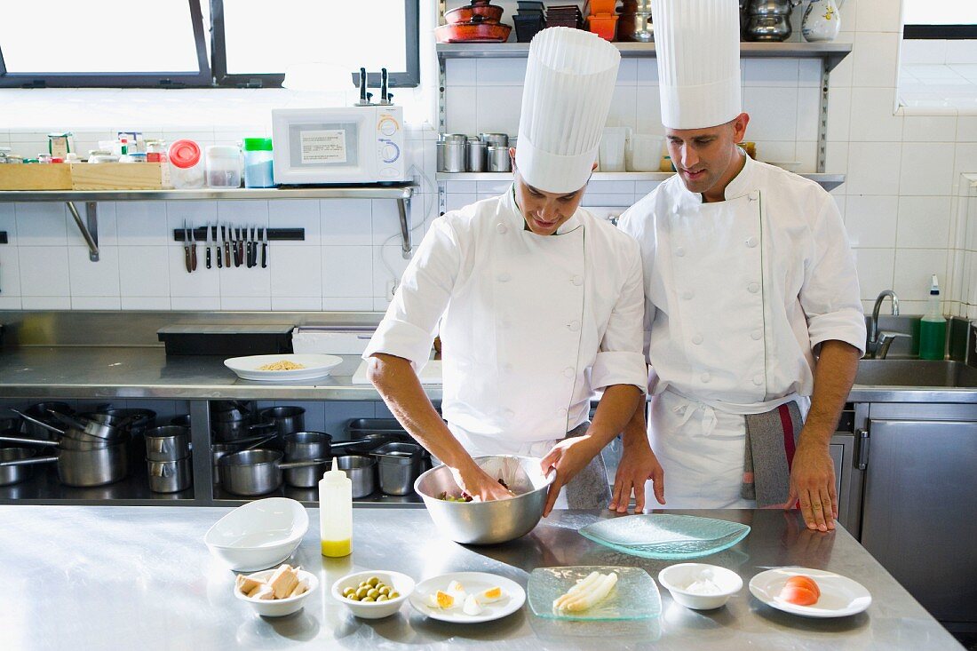 Two chefs in a commercial kitchen arranging food on a plate