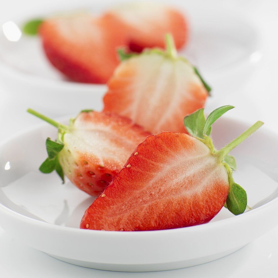 Halved strawberries in small white dishes