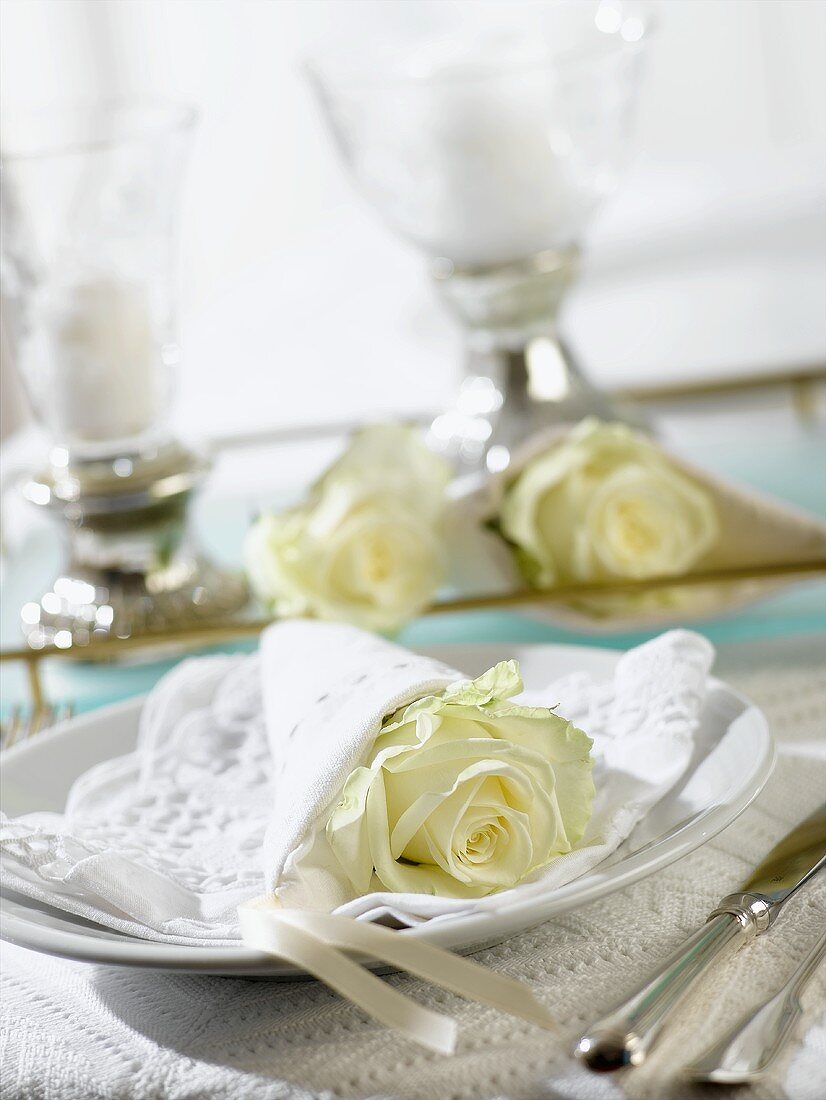 Place-setting with white rose wrapped in napkin