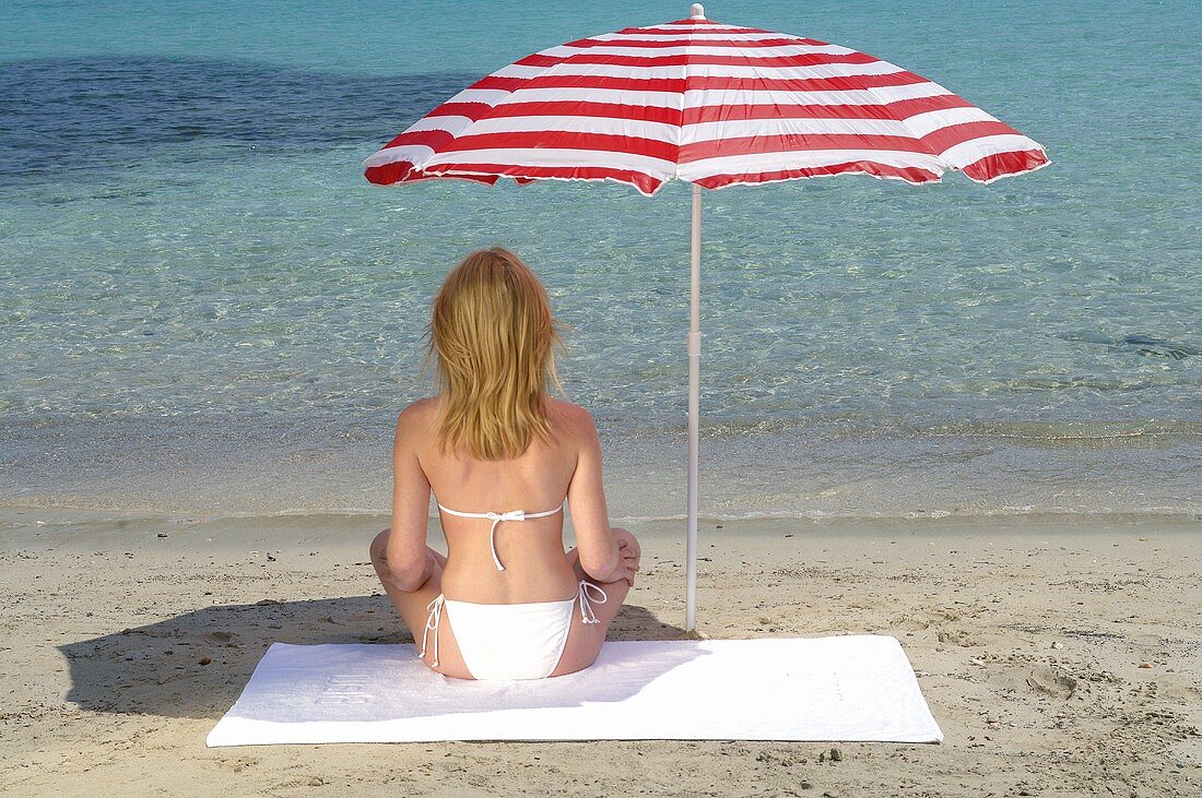 Frau sitzt am Strand unter Sonnenschirm – Bilder kaufen – 947792