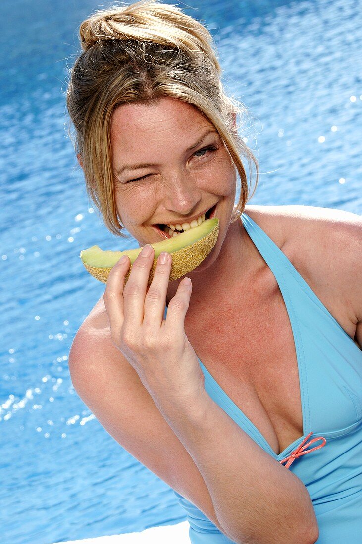 Woman biting into a piece of melon by swimming pool