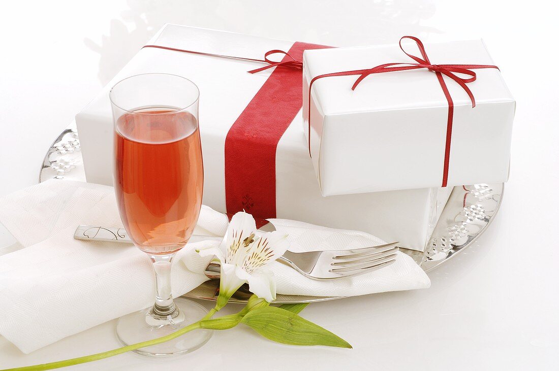 White gifts with red bows on plate, glass of sparkling wine
