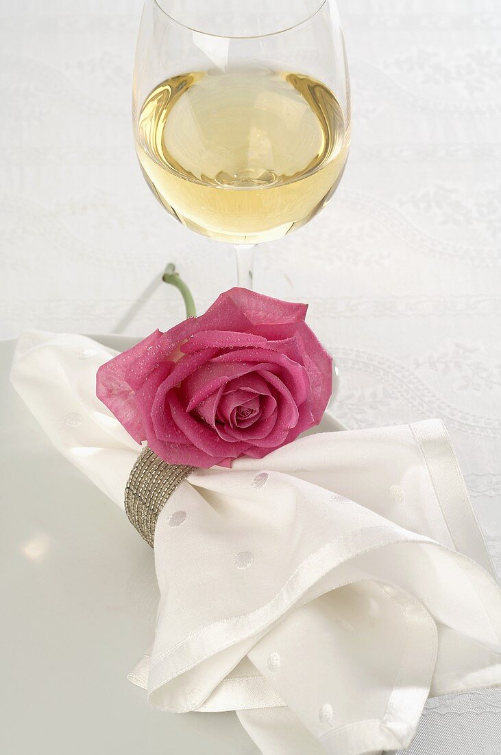 Weissweinglas und Serviette mit pinkfarbener Rose