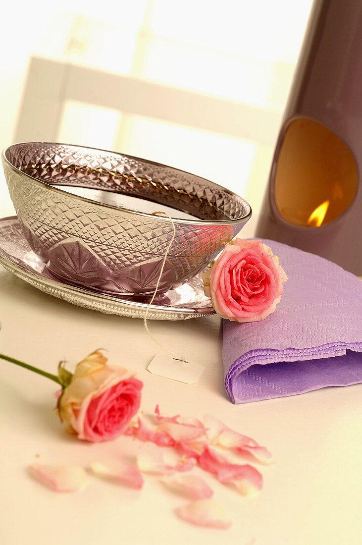 Tea in silver cup and saucer with roses, aroma lamp