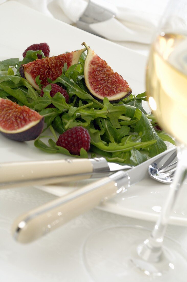 Rocket with figs and raspberries, glass of white wine