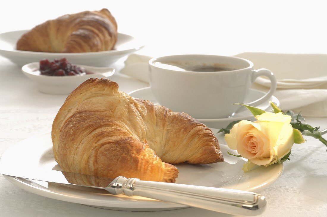 Frühstücksgedeck mit Croissant und Rosenblüte