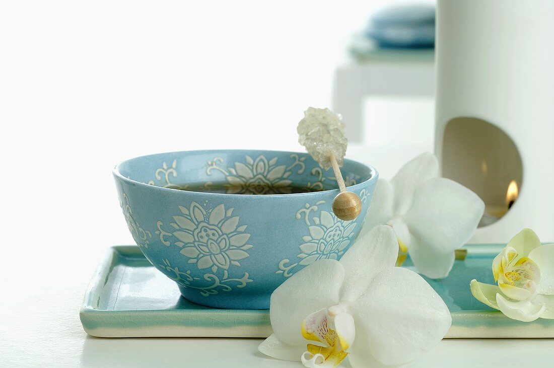 Bowl of tea with sugar swizzle stick, aroma lamp, orchids