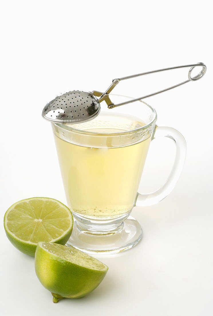 Tea infuser, glass cup of tea and lime halves
