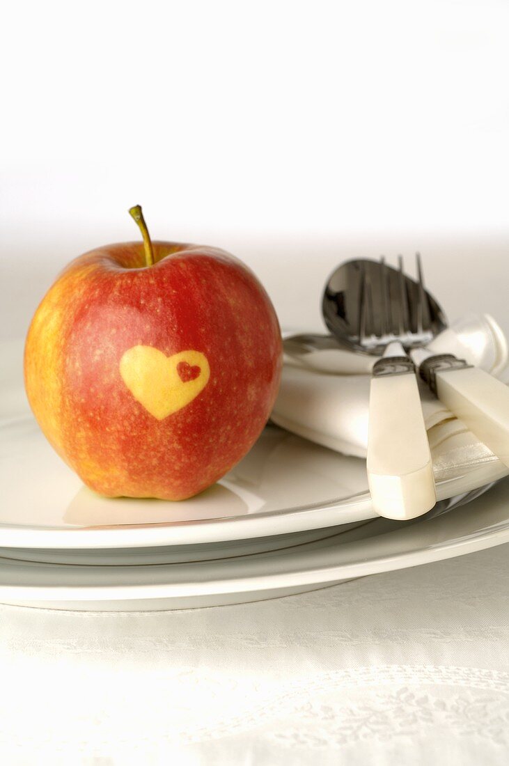 Roter Apfel mit Herz auf Teller mit Besteck