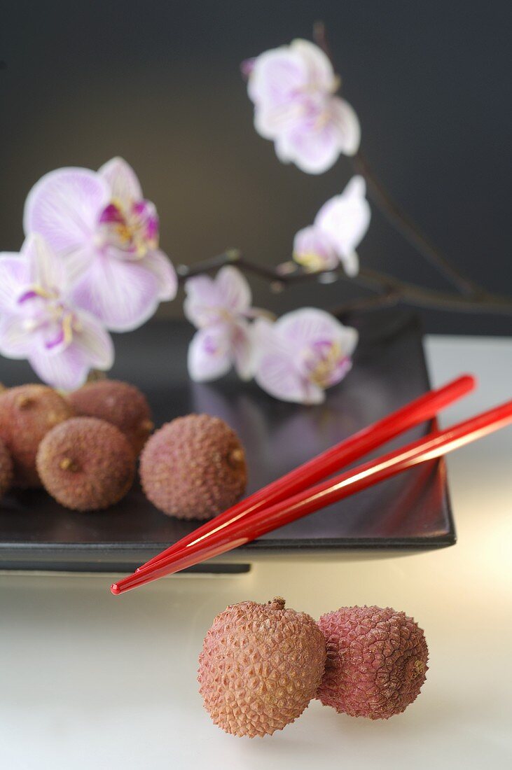 Lychees on plate with orchids and chopsticks