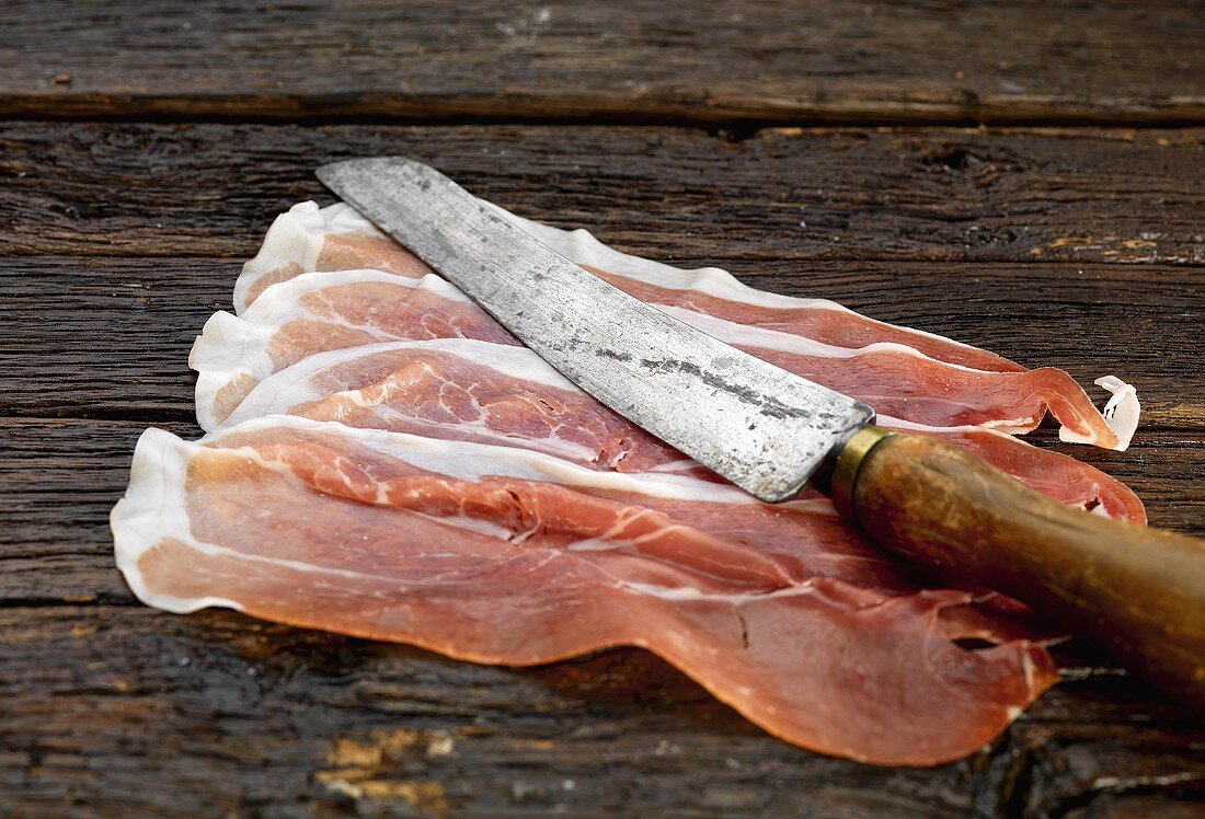 Parmaschinkenscheiben mit altem Messer auf Holzuntergrund