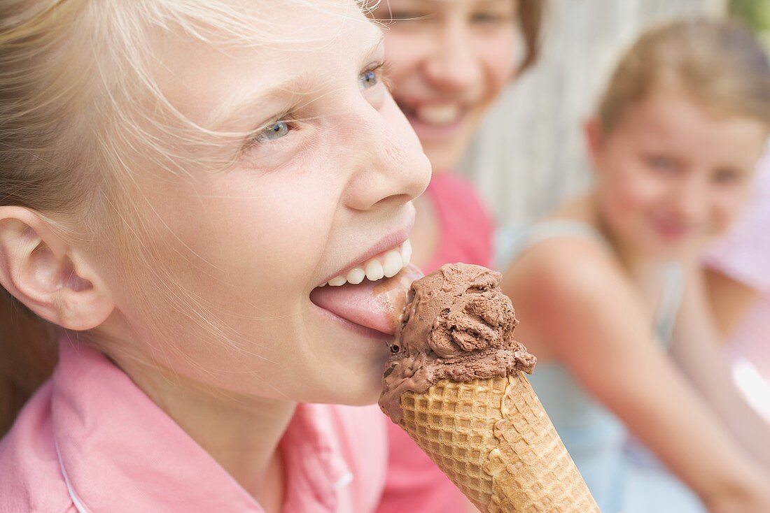 Girl licking chocolate ice cream, friends in background