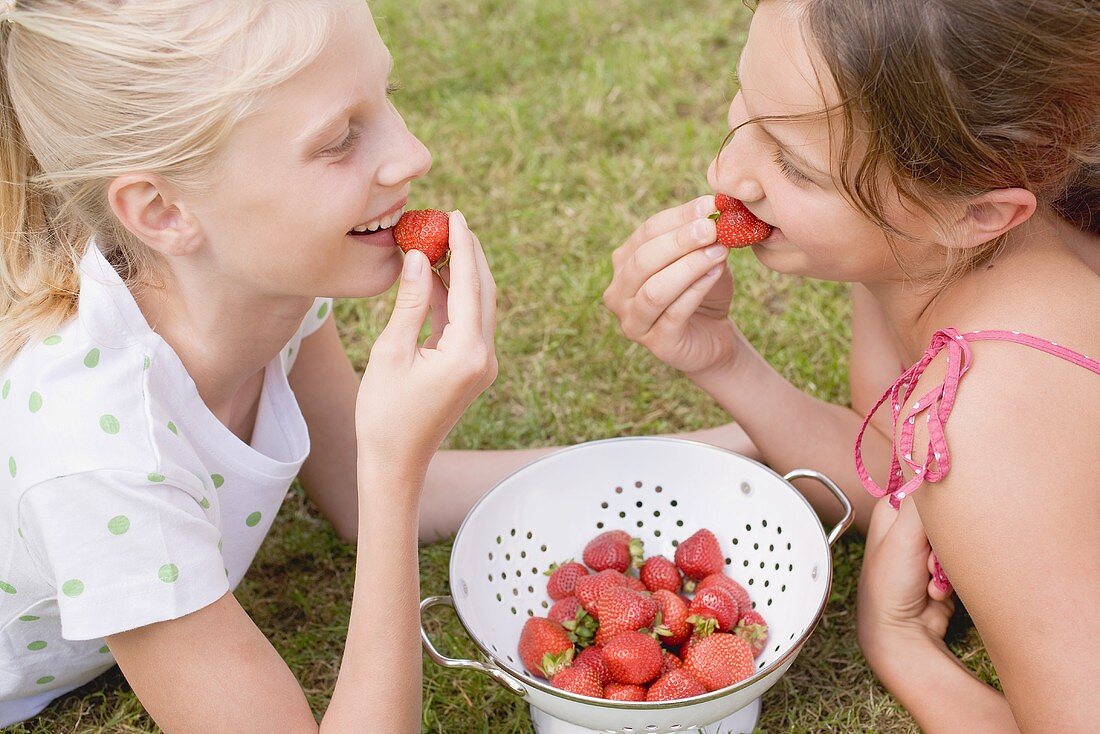 Two girls eating strawberries on grass