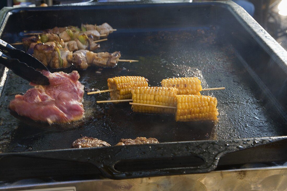 Corn on the cob, steak and kebabs in a grill pan